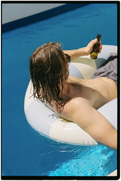 A man floating leisurely in the pool, holding a drink