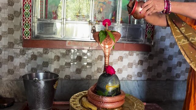 hindu woman performing abhishek ritual on sacred shivling inside temple shrine on shivratri