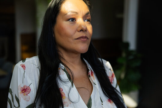 Contemplative woman in sunlight wearing floral blouse