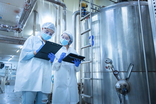 Quality control specialists auditing production standards near large stainless steel vats in industrial plant, Female engineers inspecting industrial storage tank and piping system in a factory
