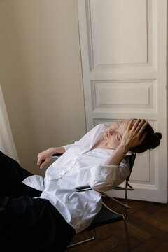 Exhausted Young Woman in White Shirt Holding Head

