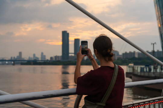 Person Taking Photos of Seoul City Skyline During Sunset on Riverbank