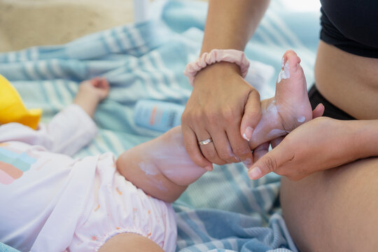Mother applying sunscreen cream on baby foot