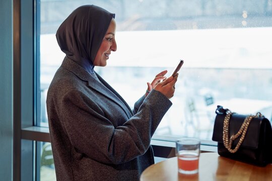Woman Using Smartphone While Enjoying a Drink in a Cafe
