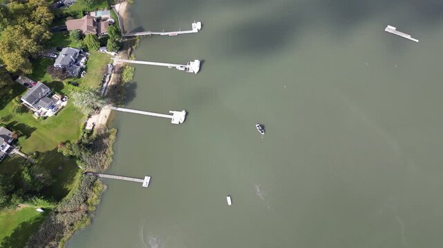Drone view ascending over a tranquil bay with numerous boats and sailboats moored, revealing beautiful waterfront properties with private docks nestled among lush green trees on a sunny day