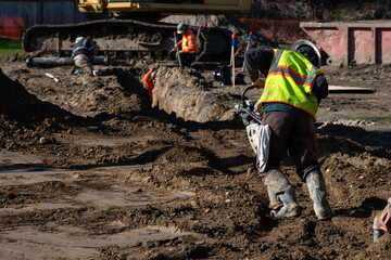Construction worker using a compactor rammer machine to manually pack the fresh dirt covering trench a newly installed water pipeline, new municipal water distribution utility project work
