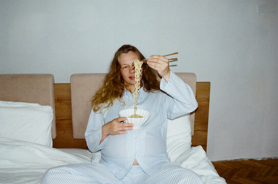 Pregnant woman enjoying noodles in bed during a cozy morning