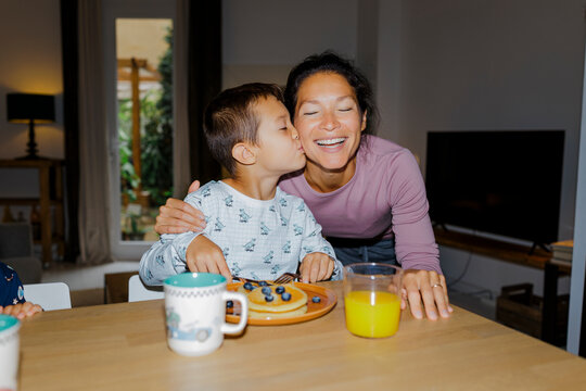Son kissing happy mother during family breakfast ugc