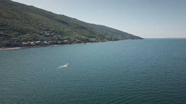 Dynamic 4K UHD drone point of interest orbit around a white motorboat on the turquoise water of Lake Garda, Italy. High-end nautical footage for luxury travel and summer lifestyle.