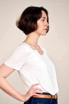 Woman in White Shirt Stands Confidently Against Plain Background