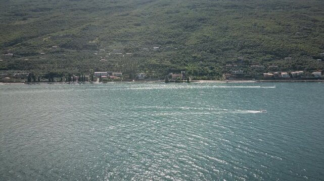 Dynamic 4K UHD drone point of interest orbit around a white motorboat on the turquoise water of Lake Garda, Italy. High-end nautical footage for luxury travel and summer lifestyle.