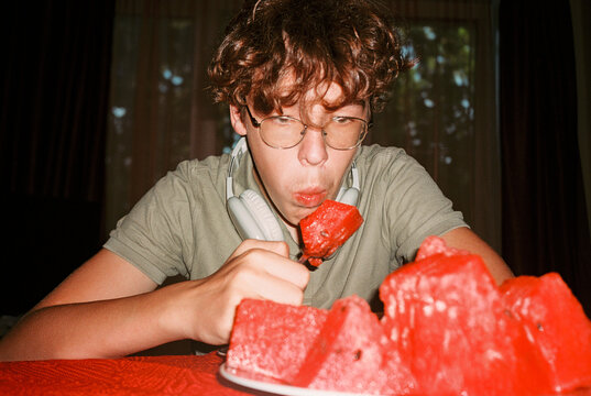 Teen boy eating watermelon slices at home table