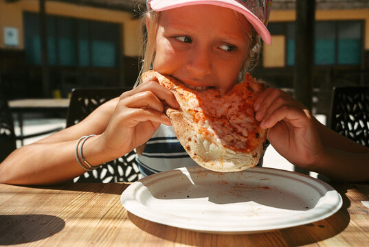 Girl eating pizza slice at wooden outdoor table