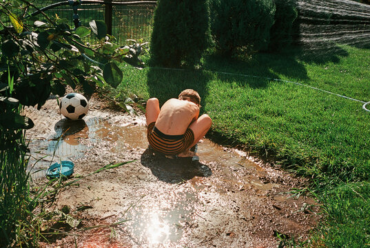 Boy playing in backyard mud puddle on sunny day