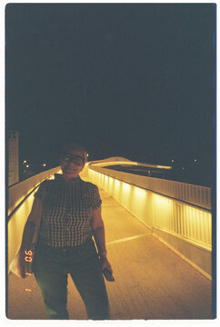 Woman Stands on Illuminated Bridge at Night in Urban Setting