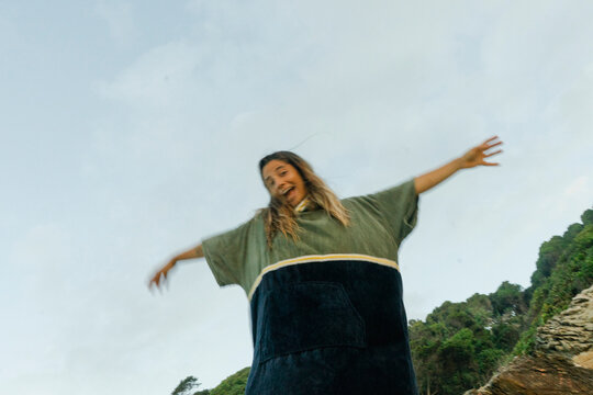 Joyful woman playing and smiling in a towel poncho at the beach