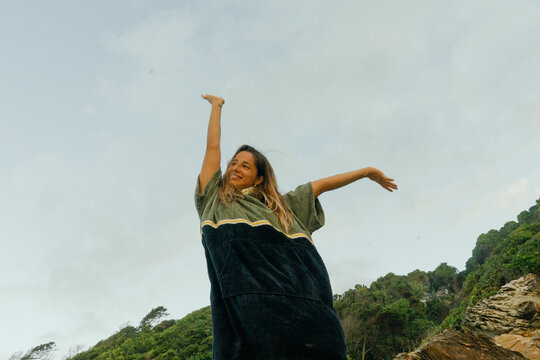 Smiling woman stretching her arms in a towel poncho at the beach