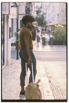 Man With Suitcase Pauses on City Street During Sunset