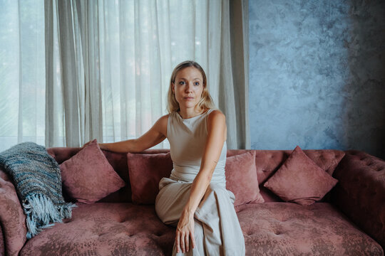 Woman Seated on a Pink Sofa in a Modern Room With Natural Light