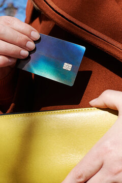 A hand takes out a bright credit card from a stylish handbag.