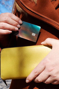 A hand takes out a bright credit card from a stylish handbag.