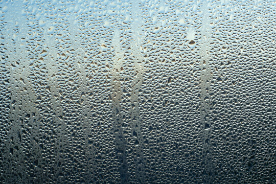 Abstract shiny bluish-dark background, texture. Water drops on glass. Wet, fogged glass, close-up.