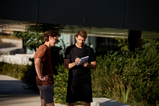 Trainer writing progress notes with client outdoors