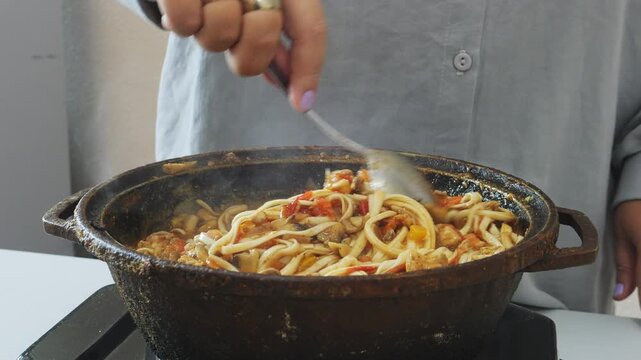 Vegetables with chicken and udon simmer in a cast iron skillet. Medium shot.