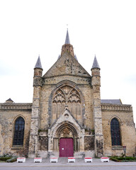 Obraz premium Front view of historic stone church with gothic arches towers and red entrance door under overcast sky Calais France