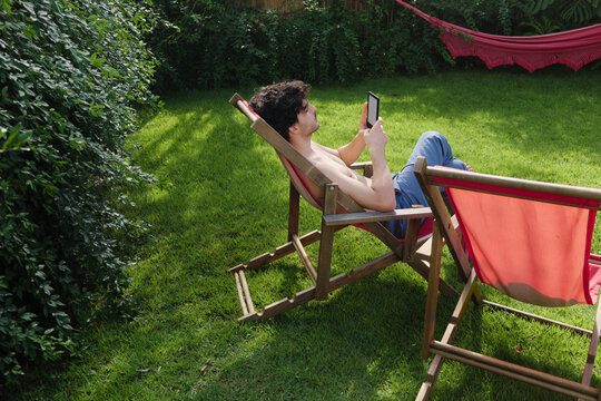 Male reading in an e-reader enjoying the sunlight in the yard
