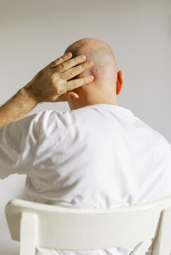 Man Sitting on Chair Touching His Bald Head in a Bright Room