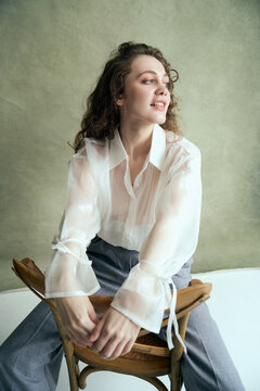 Woman in sheer blouse poses on wooden chair
