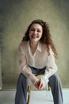Woman in sheer blouse poses on wooden chair