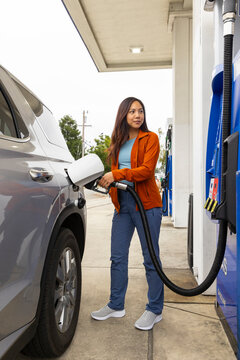 Asian woman pumping gas at station 