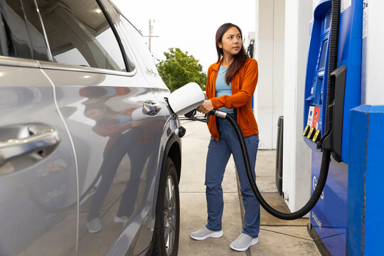 Asian woman pumping nozzle gas at station 
