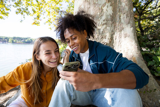 Two friends sharing earphones laughing at smartphone content