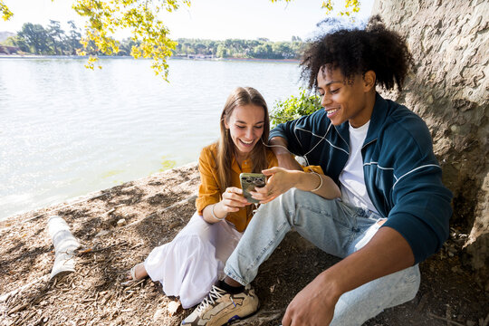 Two friends hanging out in park listening to music sharing headphones