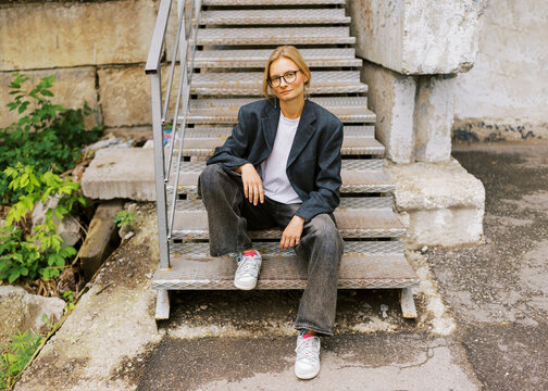 Young Woman Sitting on Metal Stairs in Urban Setting on a Sunny Day