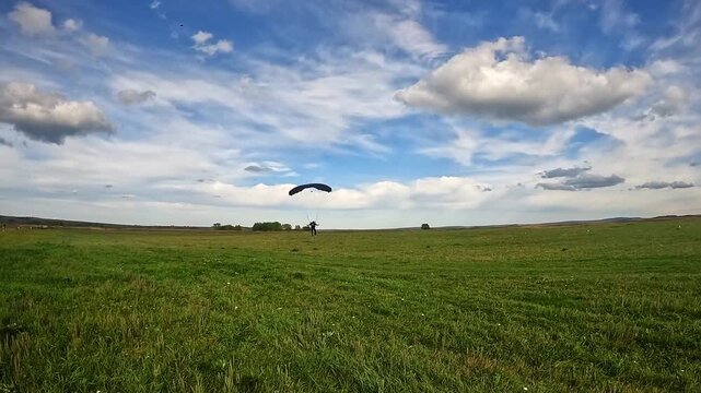 A silhouette of a parachutist with an open canopy landing against a bright sky and sun. Extreme, sport, freedom, landing zone.