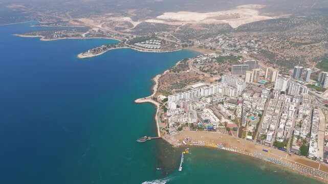 Kizkalesi, Mersin, Turkey. Bustling summer scene at beach resort with rows of umbrellas, crowded shoreline and people swimming in turquoise water.. Aerial View