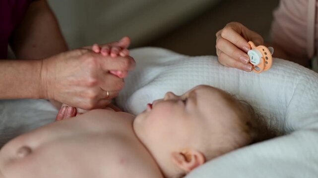 Baby lying on their back while an adult massages them and the mother gently holds the baby's hand