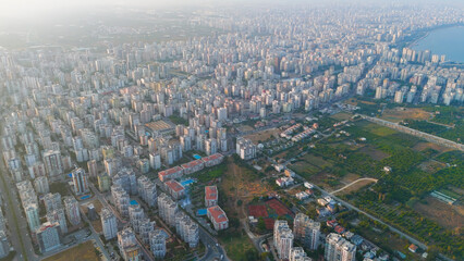 Fototapeta premium Mersin, Turkey. Aerial drone view of Mediterranean coastline at sunset. Sandy beach, sea waves, and residential district with apartment blocks in golden evening light.. Aerial View