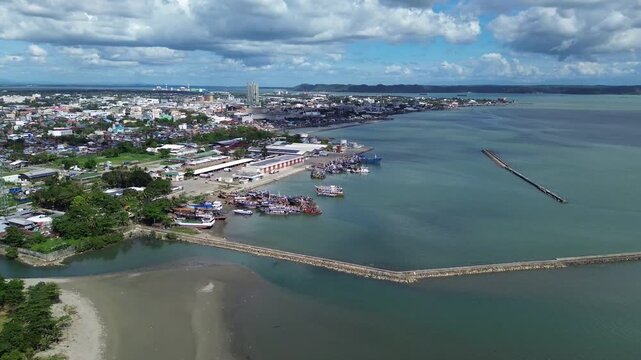 Aerial view of Iloilo City showing tropical coastline and urban skyline under dramatic clouds. Harbor with Anchored Boats, Coastal development and vibrant Philippine city atmosphere from above.