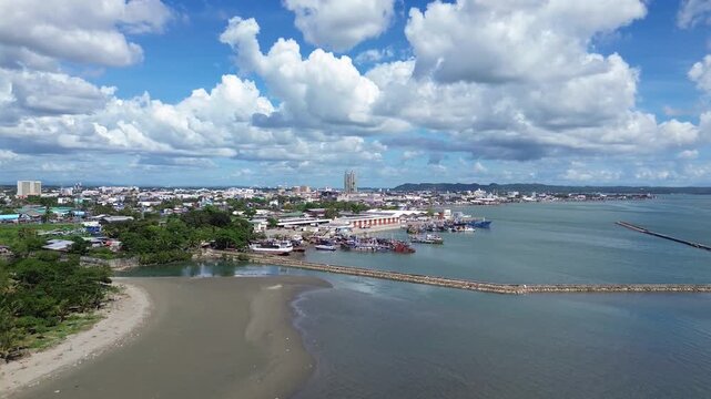 Aerial cityscape of Iloilo City Philippines showing expanding residential districts and tropical coastline under bright clouds. Dynamic urban growth and coastal development on Panay Island.