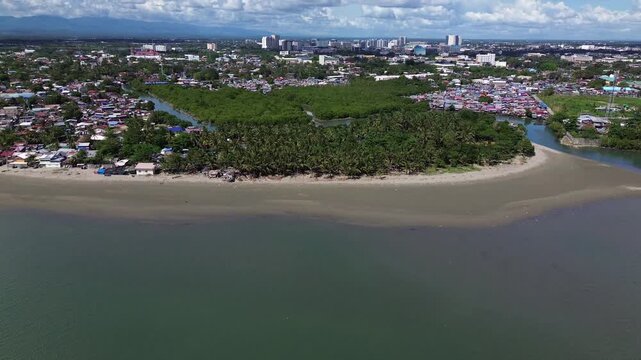 Aerial cityscape of Iloilo City Philippines showing expanding residential districts and tropical coastline under bright clouds. Dynamic urban growth and coastal development on Panay Island.