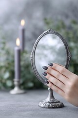 a witchs hand with black nails with antique mirror, surrounded by candles. the atmosphere is mystical, with a smoky fog in the background and dark gray and green tones