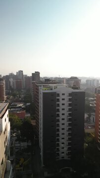 Vertical aerial pull away from skyscraper in downtown Guatemala City with white smoggy sky