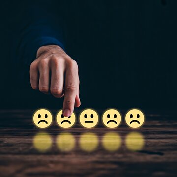 Hand choosing unhappy face emoji among customer satisfaction rating icons on dark background