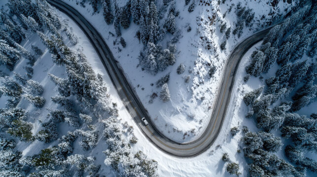 A snowy mountain road with a car driving down it. The car is in the foreground and the road is in the background. The road is winding and curvy, and the trees are covered in snow