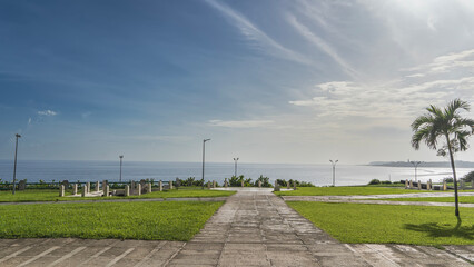 Obraz premium Park by the ocean. Paved footpaths, green grass on lawns. An ancient cannon is visible in the distance, surrounded by a fence. The barrel is aimed at the sea. Cuba. Havana. Battery of Santa Clara 